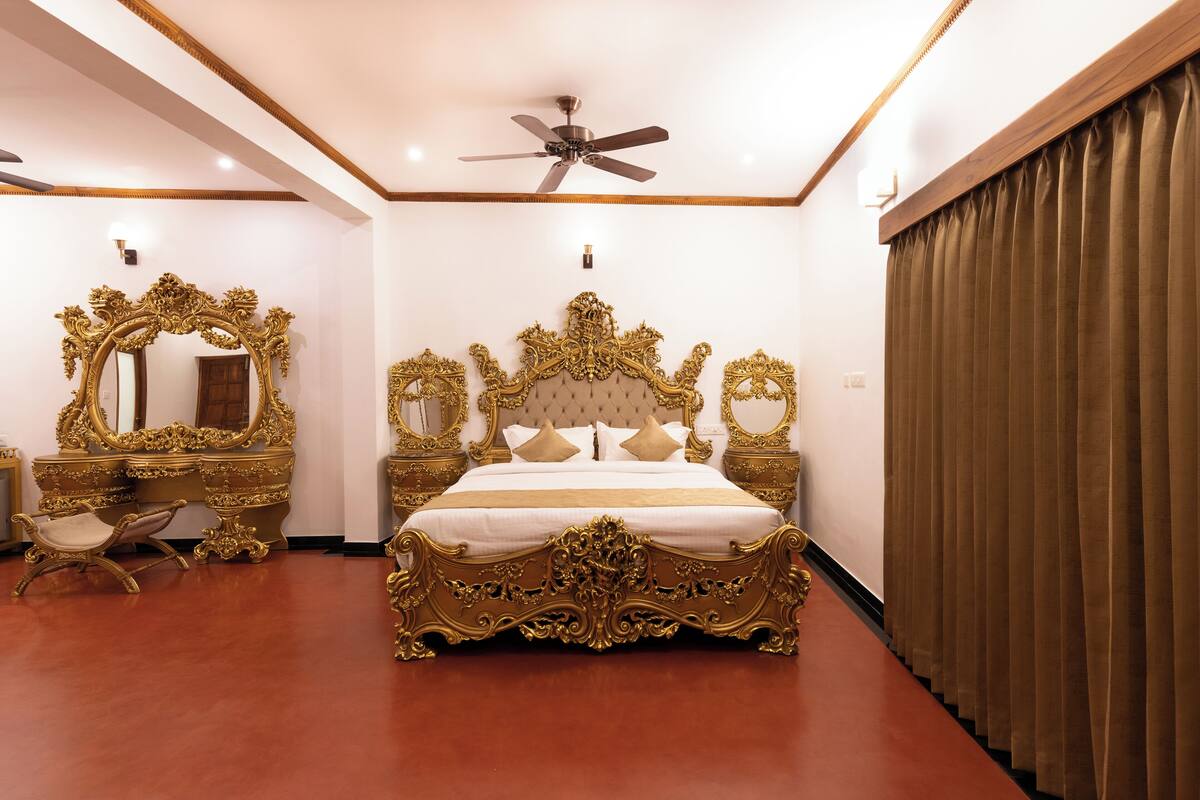 A luxurious bedroom with an ornate bed, a vanity with a mirror, and a ceiling fan.