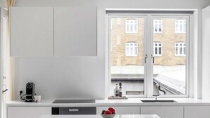 Ett modernt kök med ett stort fönster, en kaffemaskin och en skål med frukt på bänkskivan.