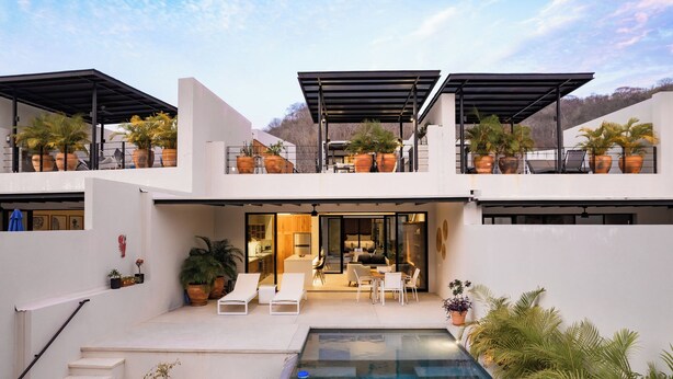 A modern two-story house with a swimming pool, outdoor seating, and potted plants.
