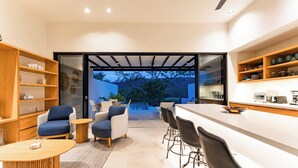 A modern kitchen with a bar area, wooden shelves, and a view of the outdoors.