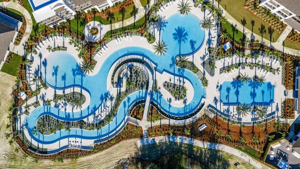 Vista aérea de un complejo turístico con varias piscinas, palmeras y un elemento acuático circular central.