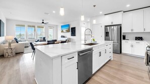 Una cocina moderna con muebles blancos, electrodomésticos de acero inoxidable e iluminación colgante.