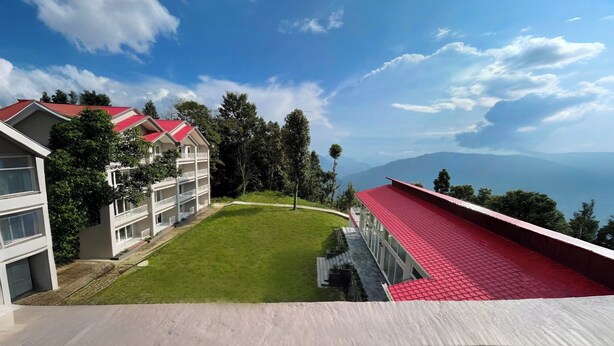 A hotel with a red-roofed building, a green lawn, and a view of mountains. - Yashshree Resorts & Spa Kalimpong (Kalimpong)