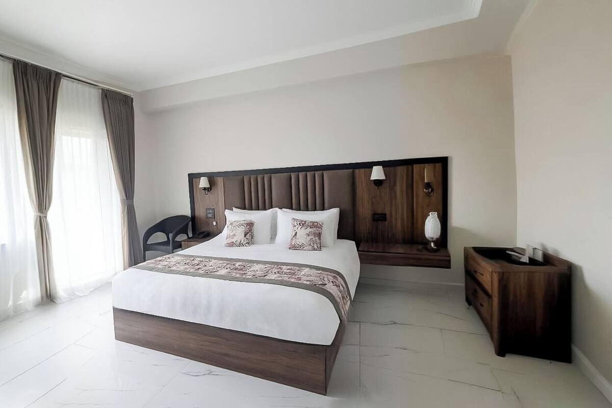 Une chambre d’hôtel moderne avec un grand lit, une tête de lit en bois, une table de chevet et une chaise.
