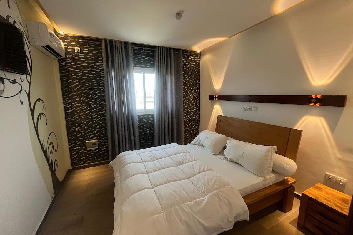A modern bedroom with a large bed, a wooden headboard, and a nightstand.