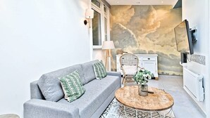 A modern living room with a grey sofa, a round wooden coffee table, and a wall mural. - Superbe appartement lumineux 6P (Paris)