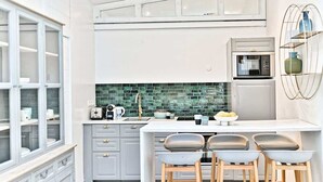 A modern kitchen with grey cabinets, a green backsplash, and a white countertop. There are two bar stools and a microwave. - Superbe appartement lumineux 6P (Paris)