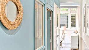 A hallway with a woven wall hanging, a door, and a glimpse of a room with a table and chairs. - Superbe appartement lumineux 6P (Paris)