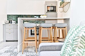 A modern kitchen with a white countertop, three wooden stools with gray bowls, a microwave, and a green backsplash. - Superbe appartement lumineux 6P (Paris)
