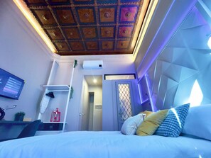 A modern hotel room with a geometric ceiling design, a bed with multiple pillows, a mounted TV, and a small desk with a plant. - Z-Archsuites - URBE (Rome)