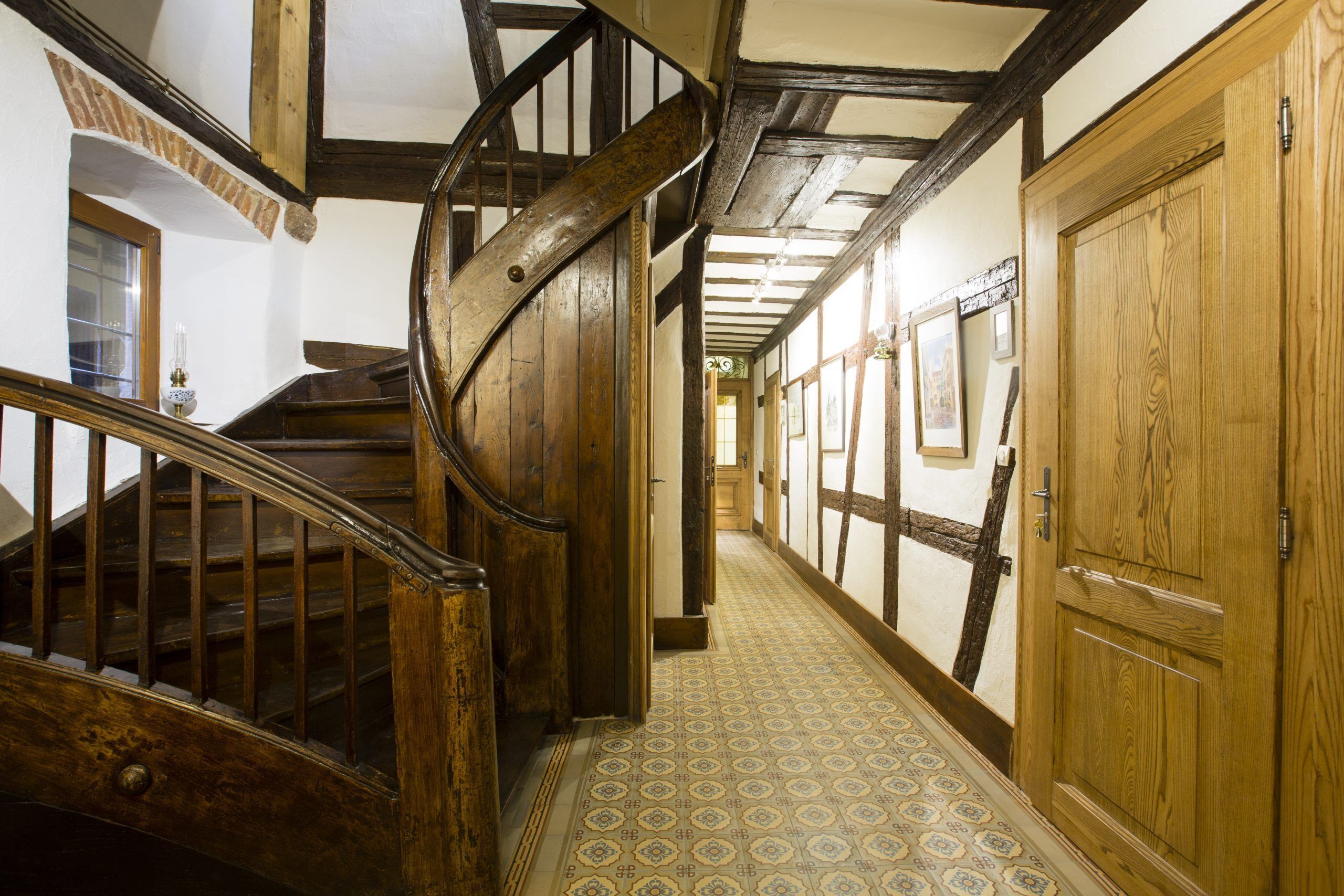 A wooden staircase with a handrail leading to a landing, a patterned floor, and wooden doors with glass panels.