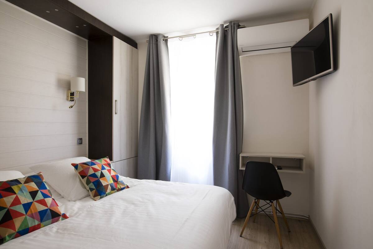 Une chambre d’hôtel équipée d’un lit, d’un bureau, d’une chaise, d’une télévision et d’une fenêtre avec des rideaux.