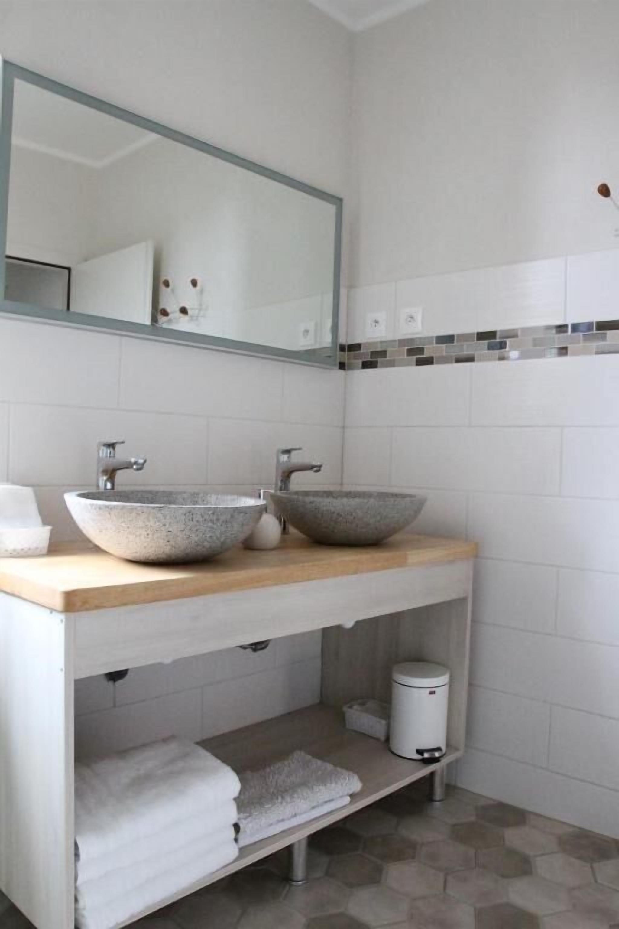Un baño moderno con dos lavamanos tipo recipiente, un espejo grande y un salpicadero de azulejos.