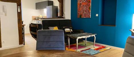 Un espace de vie compact comprenant un coin cuisine, un canapé, une petite table et un tapis coloré.