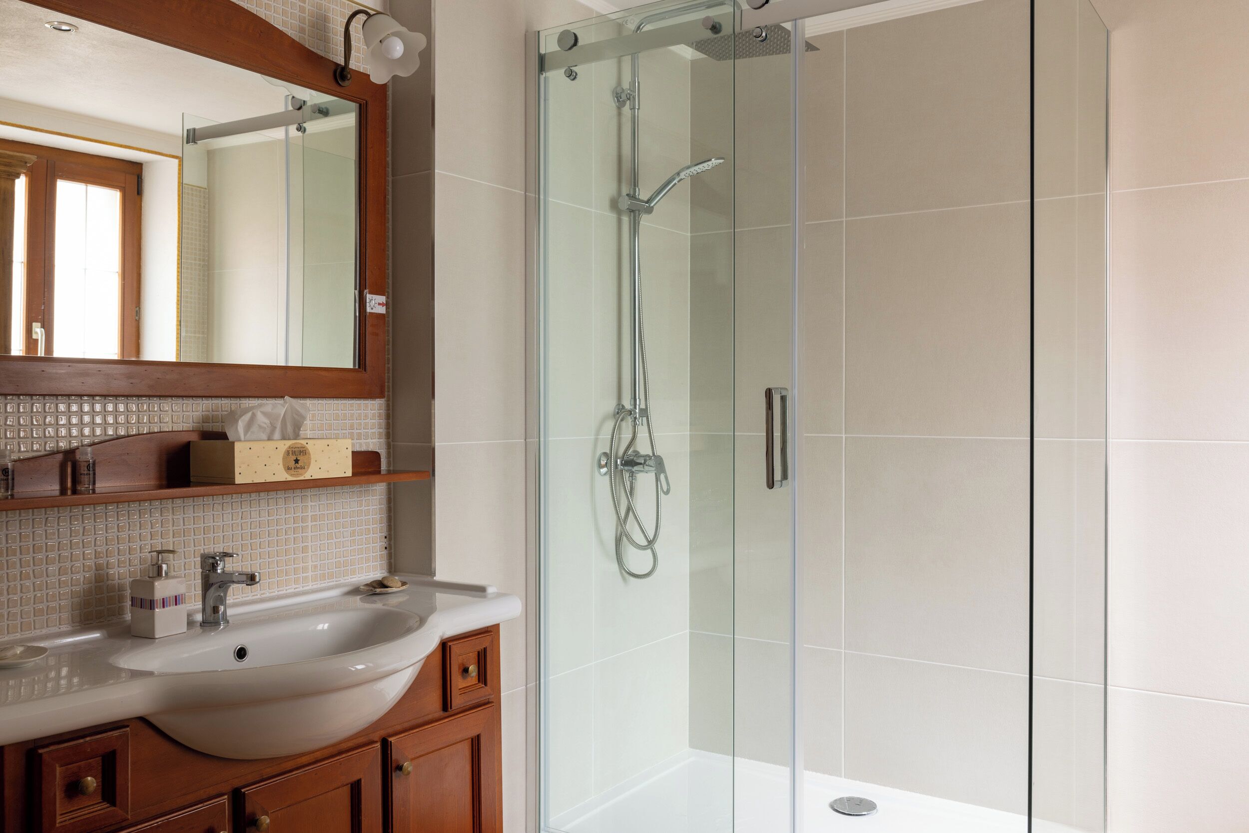 A bathroom with a glass-enclosed shower, a white sink, and wooden cabinets.
