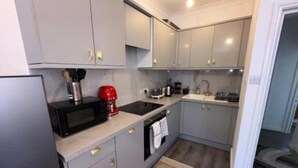 Une cuisine compacte avec des meubles gris, un four à micro-ondes, une bouilloire rouge et un grille-pain.