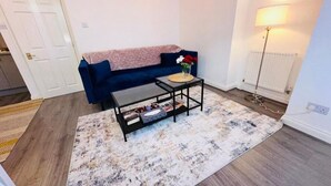 Un salon avec un canapé bleu, une table basse, un tapis à motifs et un lampadaire.