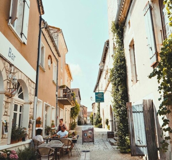 A narrow street with buildings on either side, a bar on the left, and a sign for 'art de l'art' on the right.