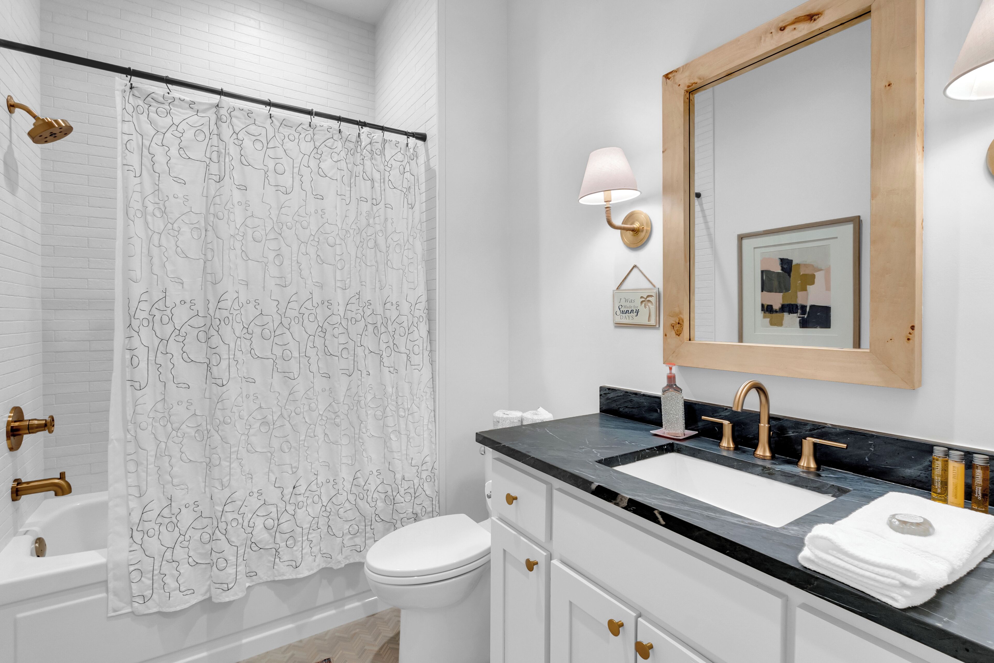 A bathroom with a white shower curtain, a white toilet, a sink with a black countertop, and a mirror with a wooden frame.