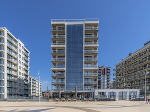 A modern multi-story hotel with a central glass facade, multiple balconies, and a ground-level restaurant. - Apartment With Panoramic sea View in De Panne (Koksijde)