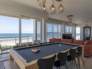 A pool table with a view of the beach, a sofa, and a TV in a spacious living area. - Apartment With Panoramic sea View in De Panne (Koksijde)