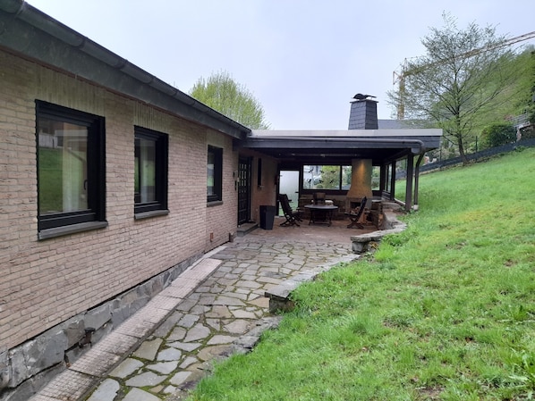 Ein Backsteinhaus mit einem Kiesweg, der zu einem überdachten Bereich mit Kamin und Sitzgelegenheiten führt.