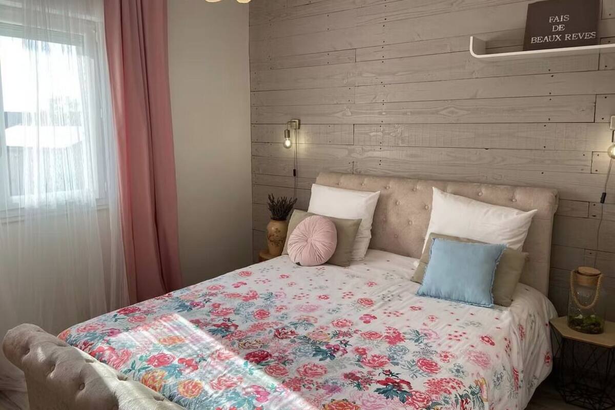Un dormitorio con una colcha estampada con motivos florales, un cabecero de madera, una mesita de noche con una lámpara y un cartel en la pared.