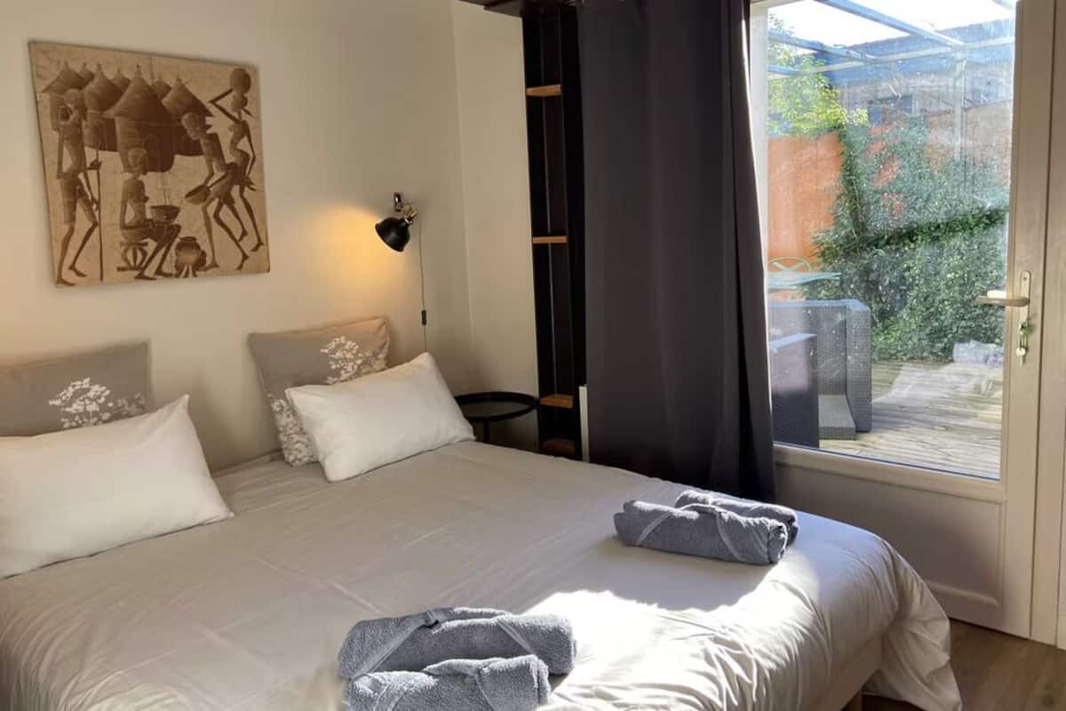 Un dormitorio con una cama grande, un cuadro en la pared, una ventana con cortinas y vistas al exterior.