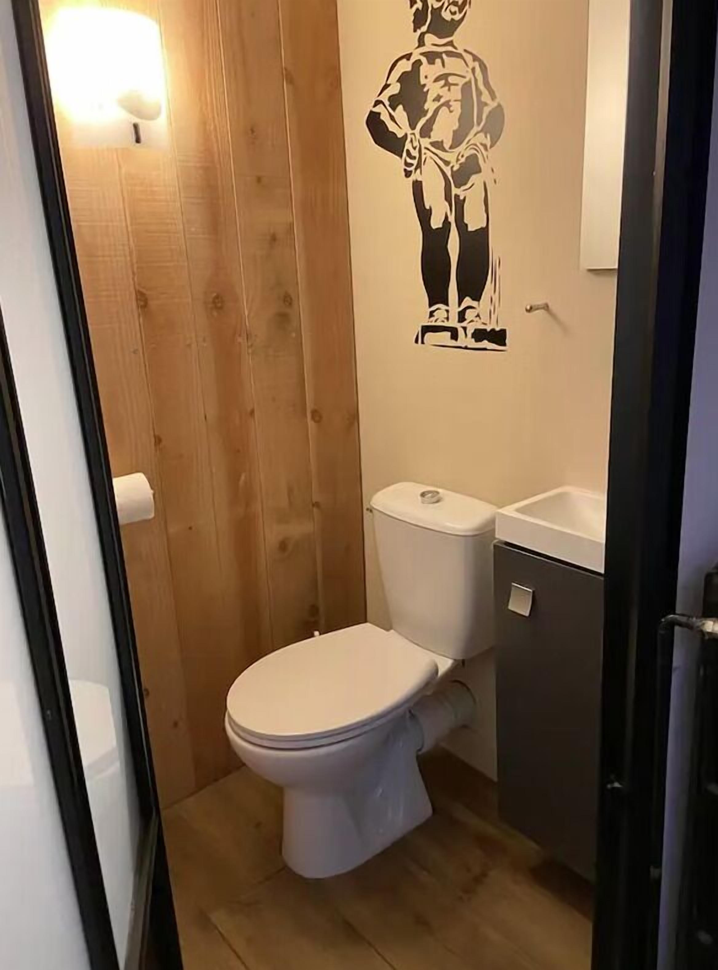 A small, compact bathroom with a white toilet, a wooden wall, and a small sink.