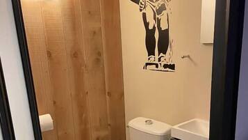 A small, compact bathroom with a white toilet, a wooden wall, and a small sink.