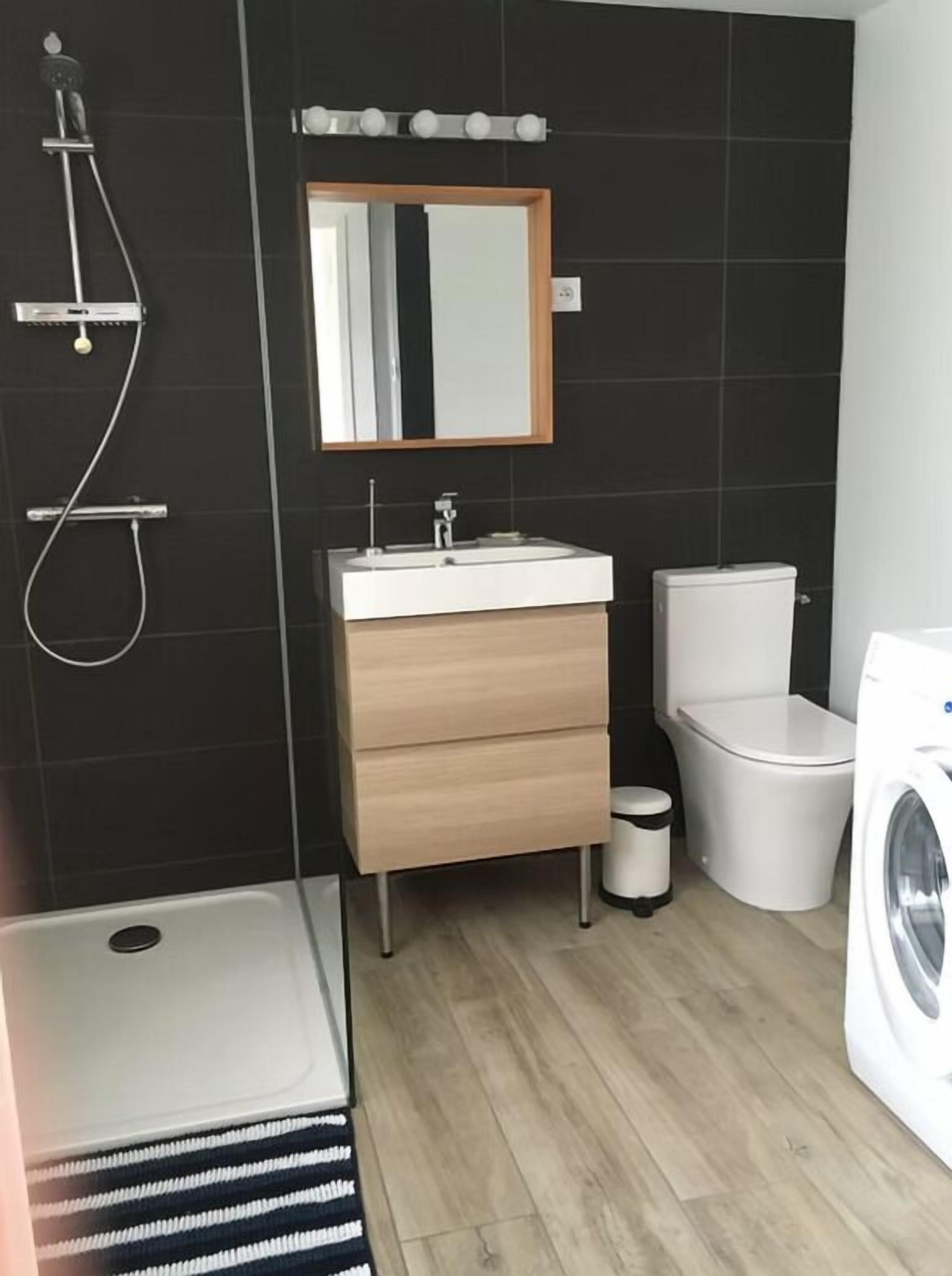 Een moderne badkamer met een douche, wastafel, toilet en wasmachine.