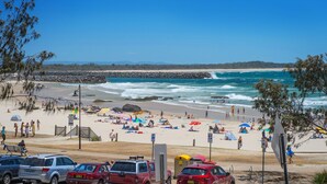 Uma praia com pessoas, guarda-sóis e carros.