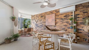 Een eetgedeelte met een bakstenen muur, een plafondventilator en een ronde tafel met stoelen.