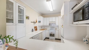 A compact kitchen with white cabinets, a microwave, a stove, and a sink.