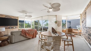 A spacious living room with a large TV, a dining area with a table and chairs, and a ceiling fan.
