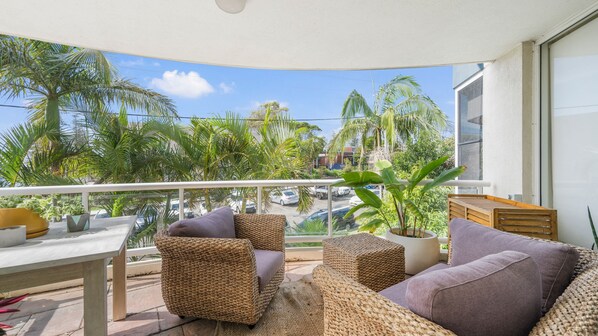 A balcony with wicker furniture, a view of palm trees, and parked cars.