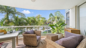 A balcony with wicker furniture, a view of palm trees, and parked cars.