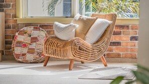 A wicker chair with cushions, a patterned rug, and a brick wall with a window.