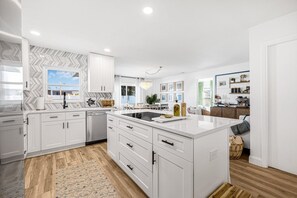 A modern kitchen with white cabinetry, a central island, and a herringbone-patterned backsplash.