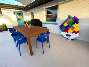 A patio with a wooden table and blue chairs, a colorful LEGO structure, and a door with a plant beside it.