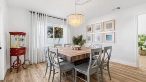 A dining area with a wooden table, grey chairs, a chandelier, and framed pictures on the wall. - Castaway Cottage: Near IMG and Beaches (Bradenton)
