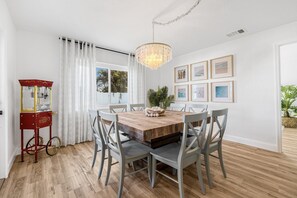A dining area with a wooden table, grey chairs, a chandelier, and framed pictures on the wall. - Castaway Cottage: Near IMG and Beaches (Bradenton)