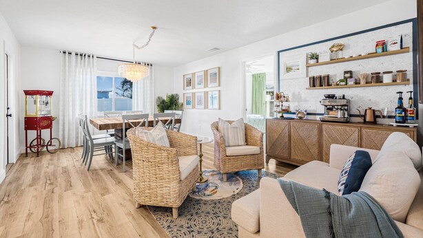 A spacious living room with a dining area, a kitchen with open shelving, and a view through a large window. - Castaway Cottage: Near IMG and Beaches (Bradenton)