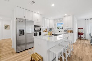 Uma cozinha moderna com armários brancos, eletrodomésticos de aço inoxidável e uma ilha central com banquetas.