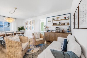 A modern living room with a dining area, wicker furniture, a white sofa, and a kitchen with shelves.