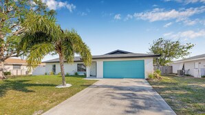 A single-story house with a blue garage door, a concrete driveway, and a small palm tree in the front yard. - Castaway Cottage: Near IMG and Beaches (Bradenton)