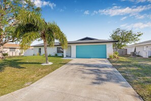 A single-story house with a blue garage door, a concrete driveway, and a small palm tree in the front yard. - Castaway Cottage: Near IMG and Beaches (Bradenton)