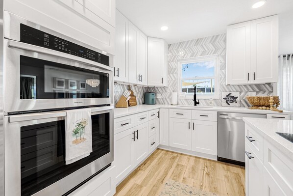 A modern kitchen with white cabinets, a stainless steel oven, and a dishwasher.