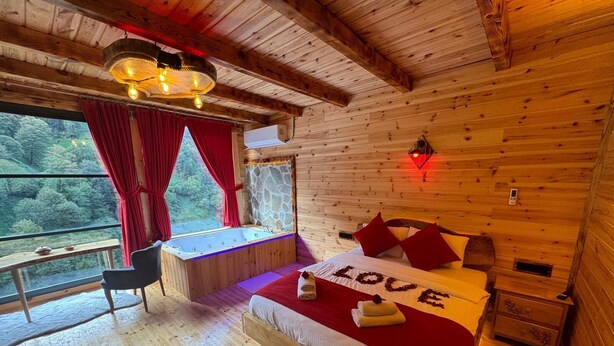 Camera da letto in una baita di legno con un letto grande, una panca, vista sulla foresta e una vasca idromassaggio.