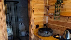 Un interior de madera con ducha, inodoro y una pequeña cocina equipada con lavabo y hervidor.